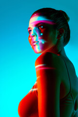 Portrait of beautiful young woman against blue background with multicolored neon reflection on...