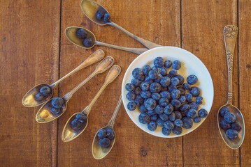 White plate and little vintage spoons wity blackberries top view on old wooden background