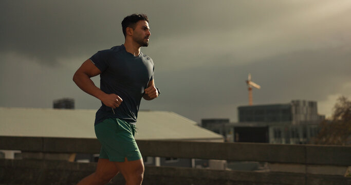 Running, city or man with workout in training, cardio jog or fitness for marathon competition. athlete, wellness or strong body for france with progress, road or health lifestyle and overcast sky