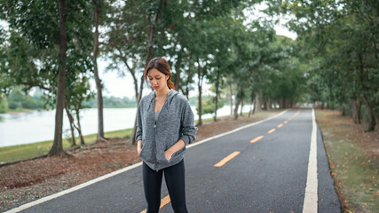 Fototapeta na wymiar Sad asian woman in hoodie running sport exercises outdoors on a background of park trees on springtime. tired