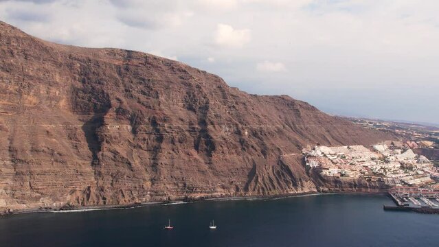 Aerial of hight mountain cliffs Los Gigantes and tourist resort on Tenerife island. Volcanic rocks, ocean, hotels in village and yacht harbor. Landmark of Canary island.