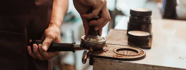 Closeup hand of barista preparation tampering ground coffee in portafilter for espresso machine....