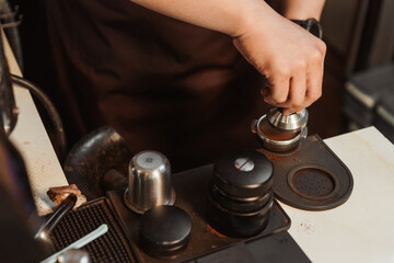 Closeup hand of barista preparation tampering coffee in portafilter for making espresso. Coffee making concept.