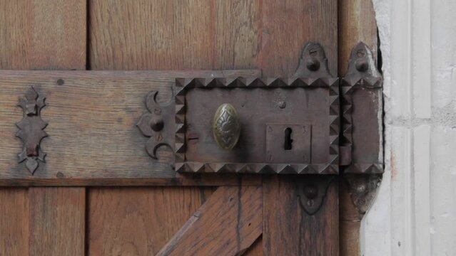 Old metal door knob on wooden door being rattled. Medieval buildings 