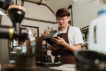 Asian man barista use digital tablet take orders service at coffee shop. Owner small business, SME business coffee shop concept.