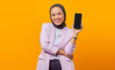 Cheerful asian woman showing smartphone blank screen over yellow