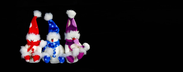 Banner with three handmade toy snowmen with hats and scarves on a black background. Christmas and New Year concept