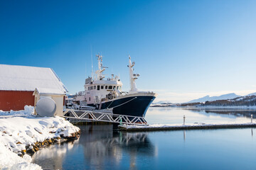 Fishing boat in harbor of Norther Norway. Red rorbu, fishing trawler and cold sea water in sunny...