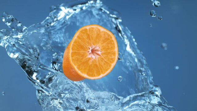Washing fresh orange fruit slices splashed by clean water droplets falling down in super slow motion on blue background