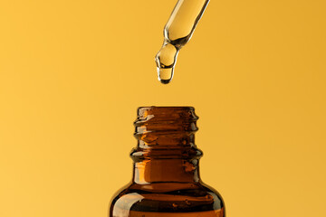 Close up of glass bottle and pipette with drop and copy space on yellow background