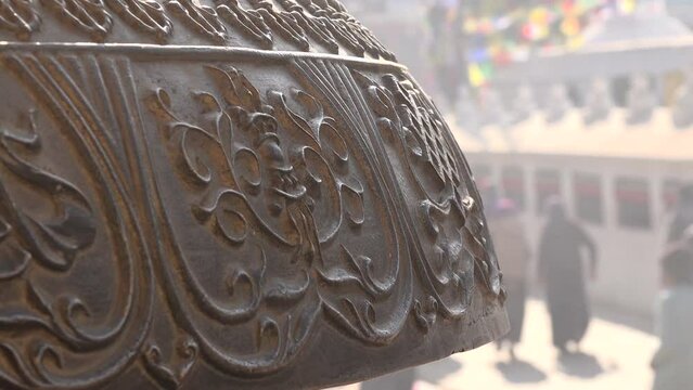 Pilgrims and others walk around the Boudhanath stupa, as visible behind a traditional Buddhist prayer bell, in Kathmandu, Nepal