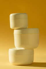 Vertical image of beauty product three cream tubs with copy space on yellow background