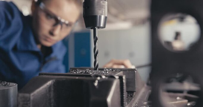 Apprentice watching drill drilling metal in workshop