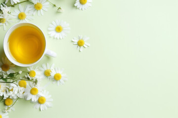 Cup of summer herbal chamomile tea surrounded by white daisy on a soft pastel yellow light copy space banner background. Top view overhead studio shot