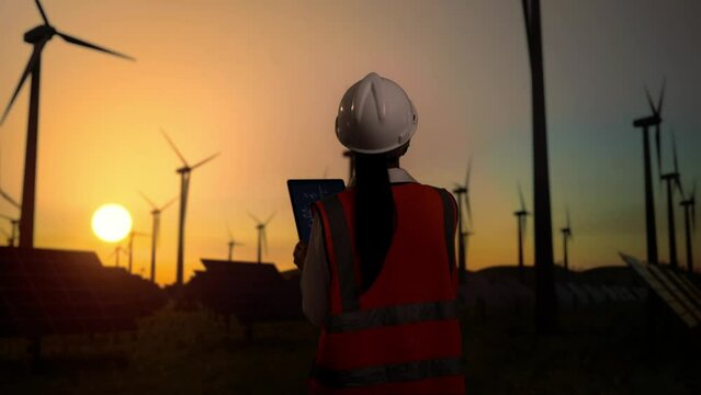 Asian female engineer looks at blueprint on the tablet in wind turbine rotating 

