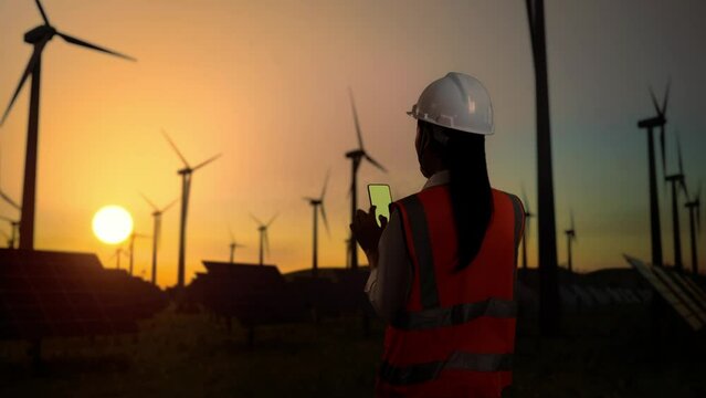 Asian female engineer works on green screen smartphone in wind turbine rotating 
