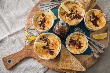 Typisches DDR Würzfleisch Ragout Fin mit Käse überbacken, Zitrone, Toast Brot und Worcester Sauce  in Auflaufform Schale auf Holz Brett, Tuch und hell grau Stein Hintergrund