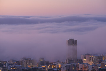 Panoramic view of clouds covering buildings at sunset in the popular city of Cape Town, South Africa with copy space. A peaceful, misty sunrise over signal hill. Landscape of a modern town at night
