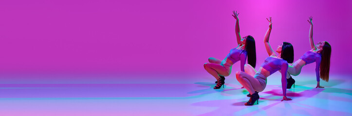 Elegant young women, attractive dancers dancing high heel dance over pink studio background in neon light. Concept of hobby, contemporary dance style, art, beauty, creativity, elegance