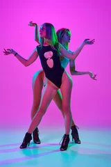 Gordijnen Art of femininity. Two elegant women dancing high heel dance over pink studio background in neon light. Concept of hobby, contemporary dance style, art, beauty, creativity, elegance © master1305