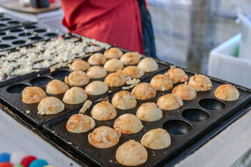 Cooking Takoyaki made of a wheat flour-based and cooked in a special moulded in a shape of little round balls containing pieces of octopus. Famous street food in Japan.