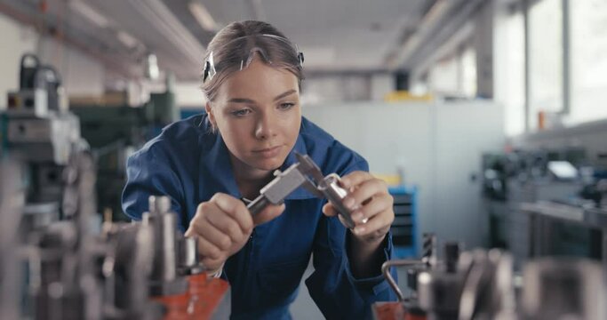 Apprentice measuring metal bolt with caliper in workshop