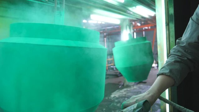 Worker spraying green paint on detail in painting chamber. Painter working at industrial manufacture. Master paint detail in specialised workshop. Man painting parts in production. Slow motion Closeup