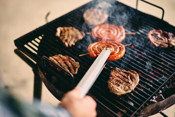 Top view of the delicious grilled meat on a barbecue, a male using a tool to switch the sides.