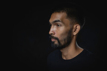 Portrait serious young man with beard looking away against a black background