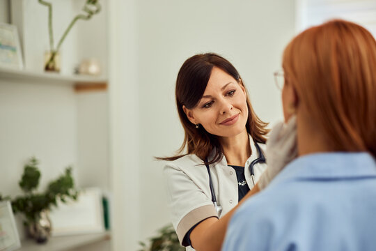 Focus on the brunette female doctor, wearing gloves and examining a ginger-haired woman.