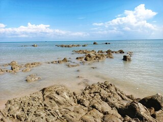 Fototapeta na wymiar Expanse Of Rocks In The Sea Of Tanjung Kalian And White Clouds and Bright Blue Sky