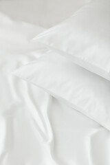 Two white pillows in satin or silk or lyocell pillowcases on white sheet. Bedding and accessories. Home textile