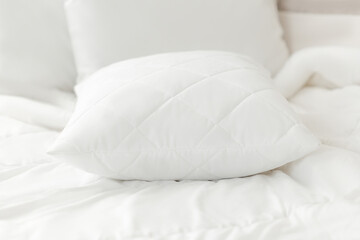 White quilted pillow on a white bedding white background. Cushion. Home textile. Close up photo