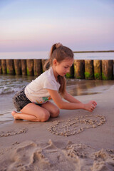 A girl on the sandy beach is drawing a heart.