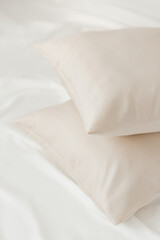 Two beige pillows in satin or silk or lyocell pillowcases on white sheet. Bedding and accessories....