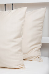 Two beige pillows in satin or silk or lyocell pillowcases on white sheet. Bedding and accessories. Home textile