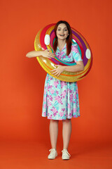 Woman wearing colorful inflatable pool tube over neck and smiling looking at the camera, isolated on orange background. Portrait of female traveler.