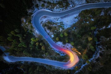 A drone view of a winding mountain road, illuminated by streaks of light from passing cars. Long exposure, dynamics and atmosphere.