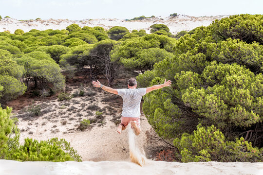 Man jumping on the sand of a dune with trees in the background.