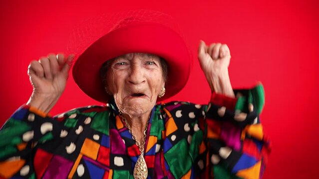Excited happy fisheye portrait of funny elderly woman with red hat and no teeth isolated on red background.