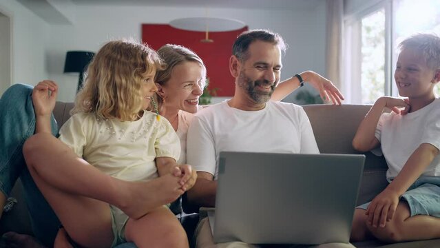 Happy family of four sitting in the living room using a laptop smiling