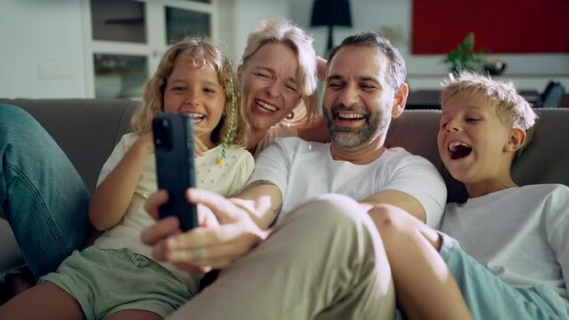 Laughing family of four sitting in the living room taking a selfie