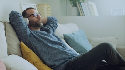 Man relaxing on sofa at home listening music with wirless headphones