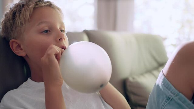 Blond boy inflating ballon sitting on sofa