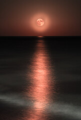 Eerie beauty unfolds as a crimson moon bleeds its light onto the rippling sea.