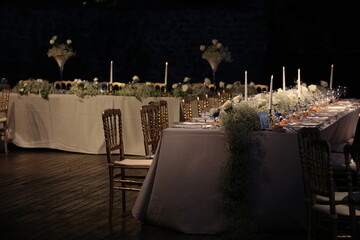 Decorated white wedding table for a festive dinner with pink flowers in brass pots on green lawn under the open sky.