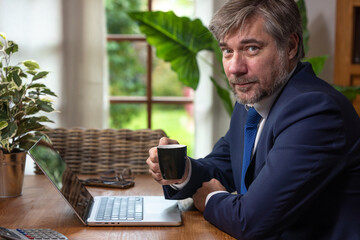 portrait d'un homme d'affaires ou employé de bureau souriant assis devant son ordinateur portable. Il boit un café en travaillant chez lui. Concept du télétravail