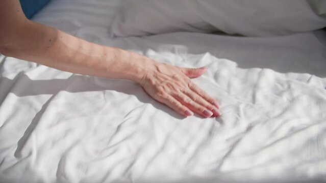 young woman cleans room and makes bed after sleeping in a white bed on a sunny morning, hand close-up
