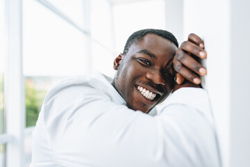 Young african man in white shirt and glasses posing near large window