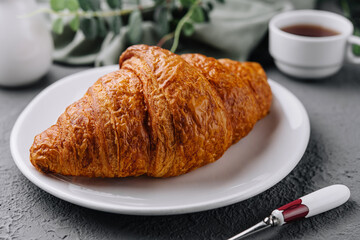 A fresh croissant on plate and cup of tea